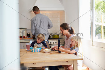 Kids and mum at table, dad cooking, three quarter length