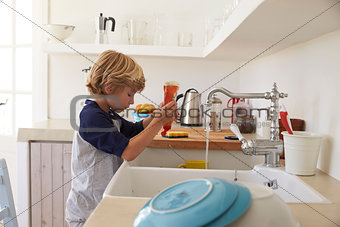 Boy squeezing washing up liquid into sink to wash dishes