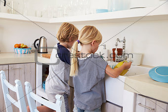 Brother and sister kneeling at sink to wash up in kitchen