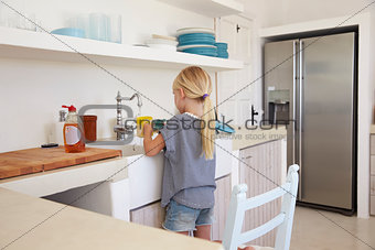 Young girl kneeling on chair washing up, back view
