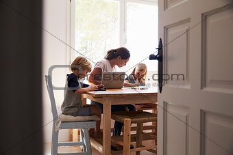 Mum and two kids working in kitchen, close up from doorway