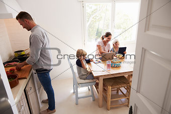 Dad cooking and mum with kids at the kitchen table