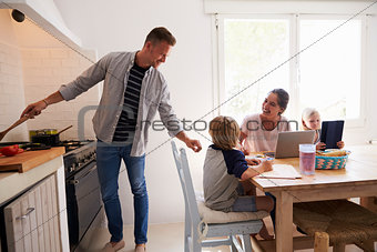 Dad cooking turns to mum with kids at the kitchen table