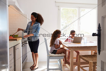 Mum cooking while kids work at kitchen table, from doorway
