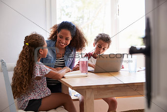 Mum sitting with kids at kitchen table, son using laptop