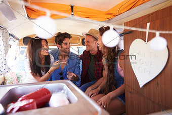 Four friends on a road trip talk in the back of a camper van
