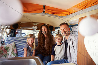 Smiling family sitting in the back of vintage camper van