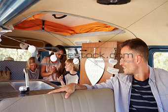Dad in driving seat of camper van looks back at his family