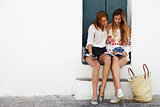 Female friends sitting in doorway reading a guidebook, Ibiza