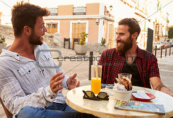 Two male friends taking at a table outside a cafe in Ibiza