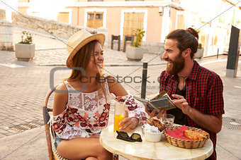 Laughing couple reading a guidebook outside a cafe in Ibiza