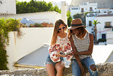 Two female friends sitting on wall reading guidebook, Ibiza