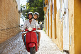 Couple riding motor scooter in old Ibiza street, front view