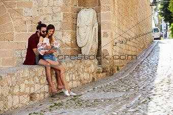 Man embracing his girlfriend on a wall, reading a guidebook