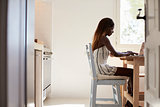 Young woman sitting in her kitchen using laptop computer