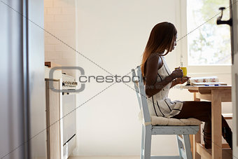 Young woman sitting in kitchen reading and drinking coffee