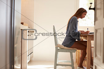 Young woman writing at the kitchen table, full length, Ibiza