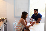 Mixed race couple sitting in kitchen and drinking wine