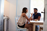 Young adult couple sitting in kitchen smiling, drinking wine