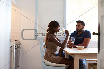 Young adult couple sitting in the kitchen drinking wine