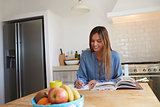 Young woman at kitchen table with recipe book writing a list