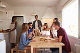 Group of friends talk in kitchen, one preparing food