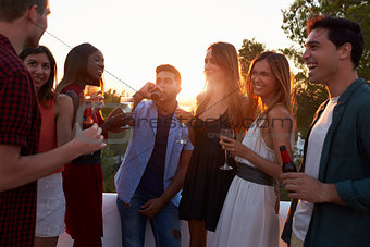 Adult friends socialising at a party on a rooftop at sunset