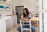 Teenage girl sitting in kitchen using smartphone, front view