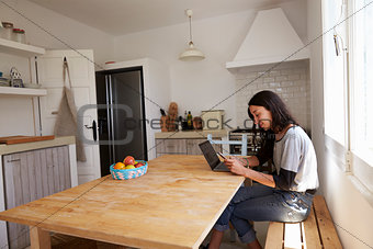 Smiling girl with laptop, reading message on phone in kitchen