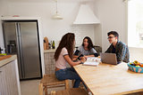 Three teens talk as they study in a kitchen using a computer