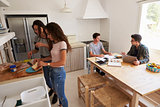 Four teenagers making lunch and studying together in kitchen