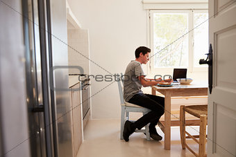 View from doorway of teenage boy studying in a kitchen