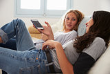 Two teenage girls relax, talking together at home