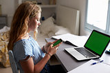 Teenage girl using smartphone at a desk in her bedroom