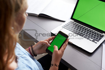 Girl using phone at desk in her bedroom, over shoulder view