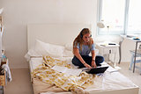 Teenage girl doing homework sitting on her bed with laptop