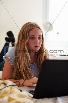 Teenage girl using laptop lying on her bed, vertical