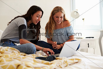 Two teenage girls on bed using laptop, surface level view