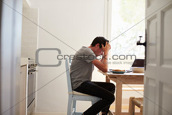 View from doorway of unhappy teenage boy studying in kitchen