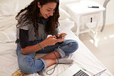 Teenage girl sitting on bed text messaging, elevated view