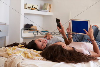 Teenage girls lying on bed talking and using technology