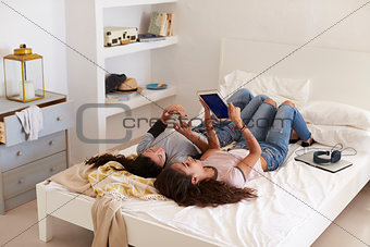 Two girls lying on bed using phone and tablet, elevated view