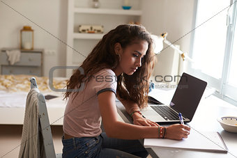 Teenage girl doing homework at a desk in her bedroom