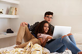 Teenage couple hanging out in bedroom watching laptop