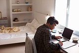 Teenage boy in headphones at desk in bedroom, elevated view