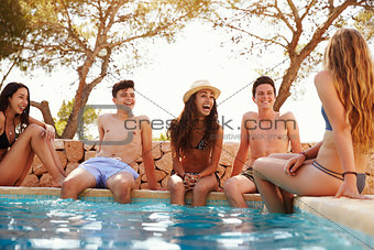 Teenage friends sitting at the edge of a swimming pool
