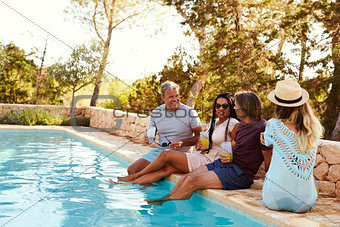 Two couples sitting at the edge of a swimming pool talking