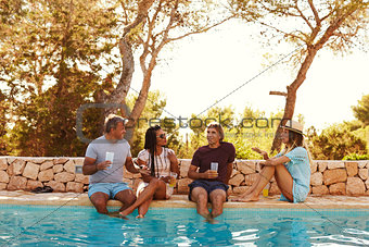 Two couples sit at poolside talking, front view