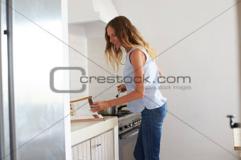 Woman reading recipe book and preparing food in kitchen