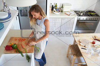 Woman standing in kitchen chopping vegetables, full length